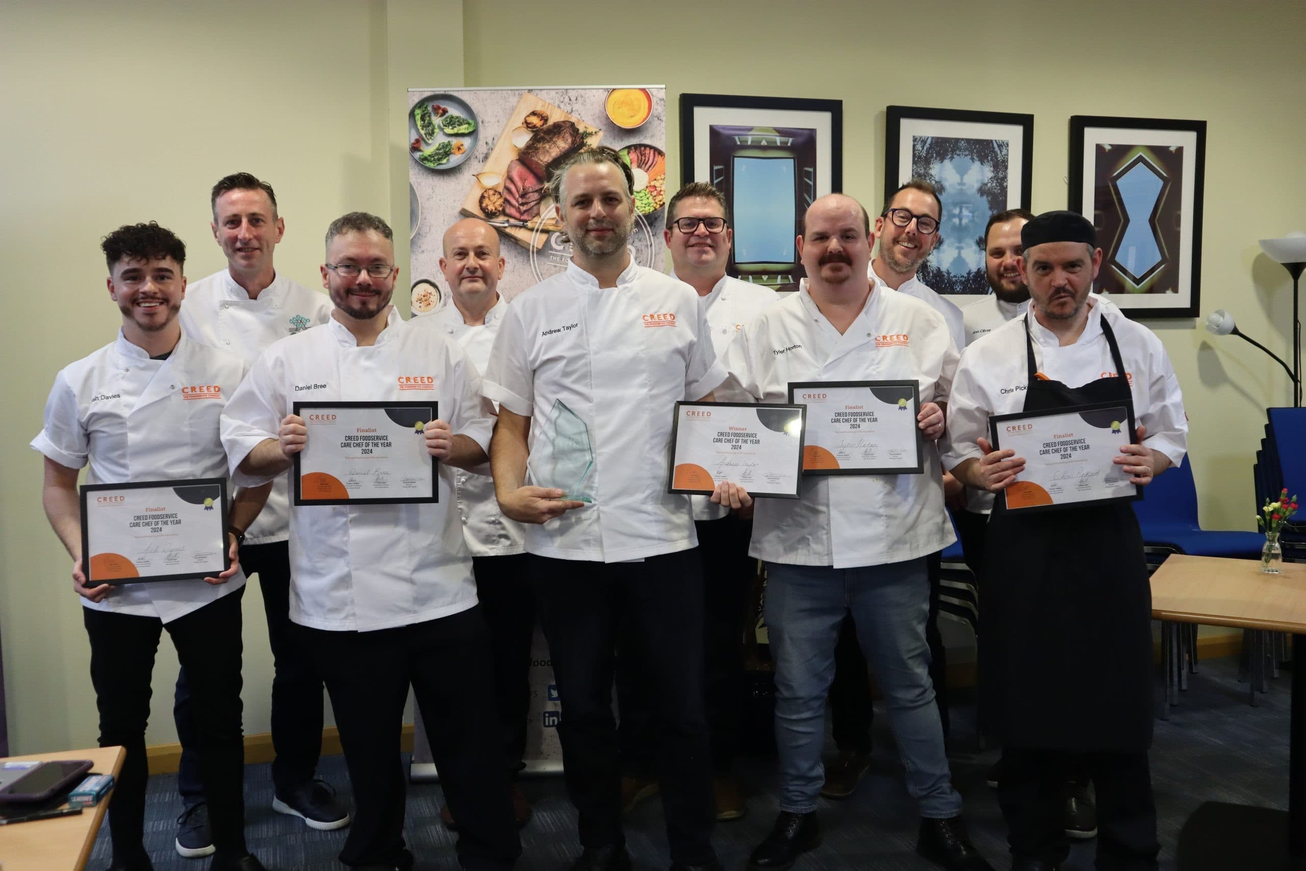 Group photo of ten chefs in white chef coats holding CREED certificates and awards in an indoor setting